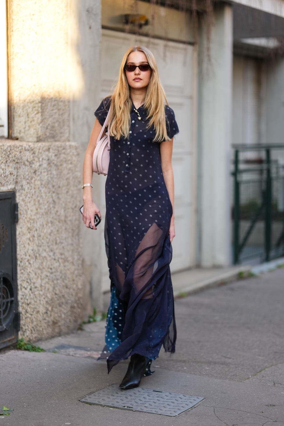 paris, france march 05: a guest wears dark brown sunglasses, black white polka dotted half buttoned short sleeve sheer mesh maxi dress, light pink leather bag, a silver bracelet, shiny black pointed toe heels leather shoes, outside acne studios, during the paris fashion week womens fall/winter 2025 2026 on march 5, 2025 in paris, france. (photo by edward berthelot/getty images)