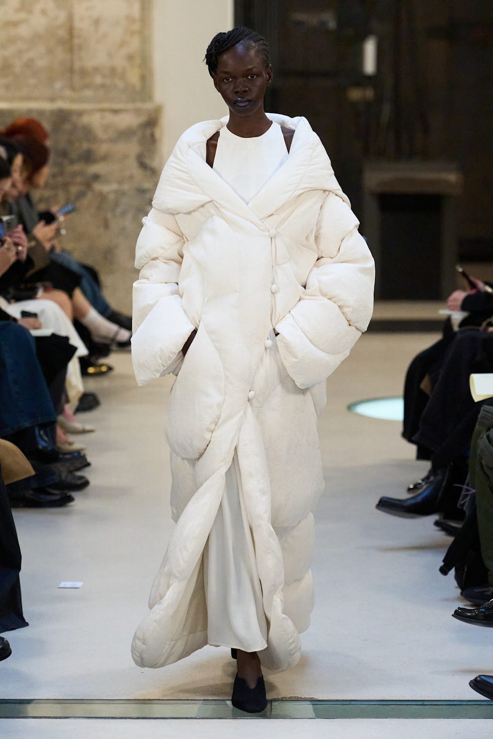 A model walks down a runway wearing an oversized white quilted coat