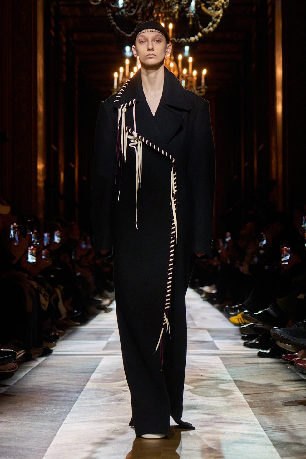 Runway model wearing a contemporary black coat with unique detailing