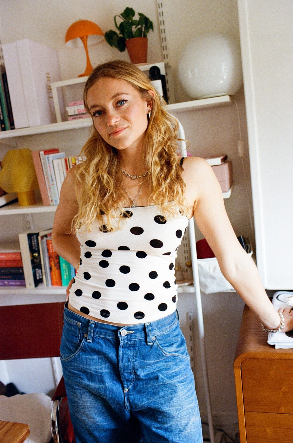 a person wearing a polka dot top and denim jeans stands in a cozy indoor setting