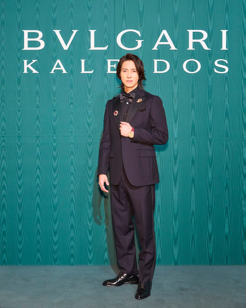 a formal event scene featuring a stylishly dressed individual against a branded backdrop