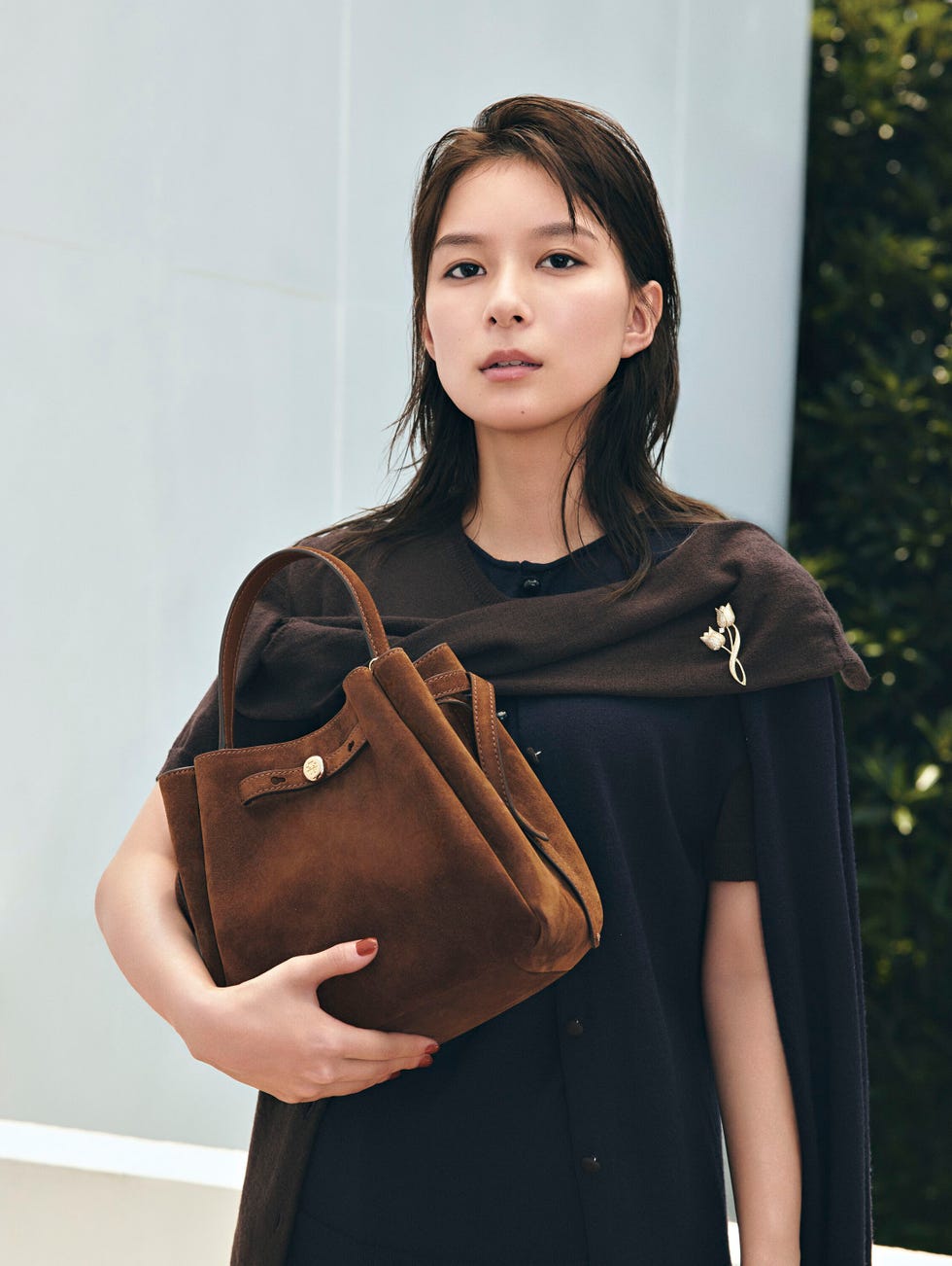 a person holding a brown suede handbag while wearing a dark outfit and a brown wrap