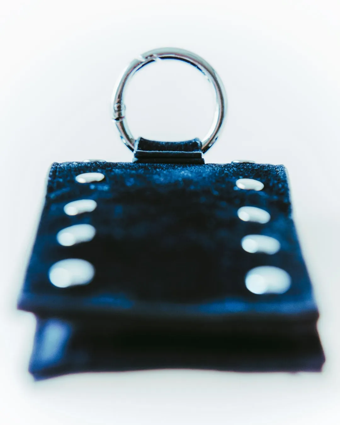 黒い革製のクリップ。上部には丸い金属製のリングが付いている。背景は白で、クリップが強調されている。