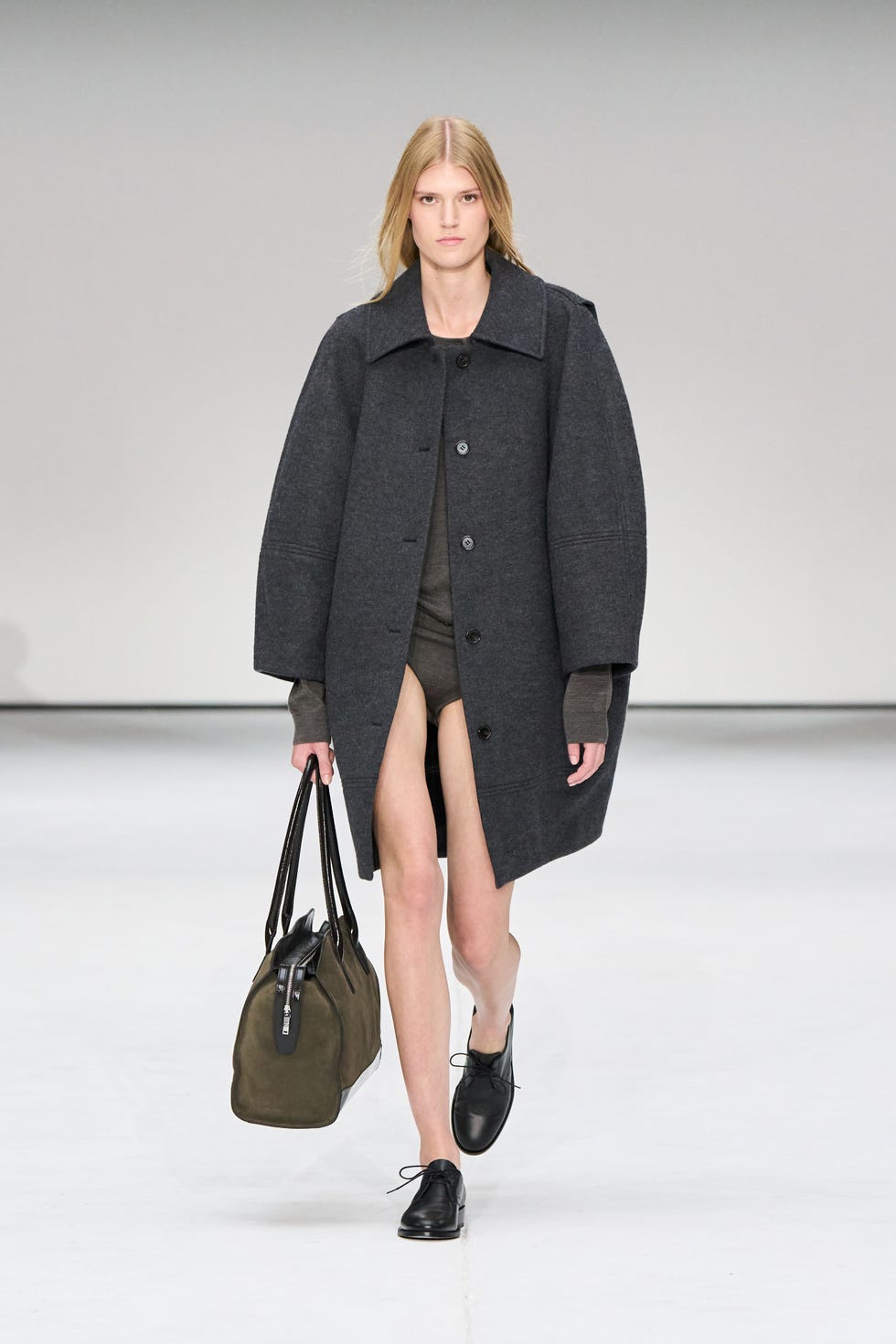 fashion model showcasing an oversized dark gray coat accompanied by a green handbag