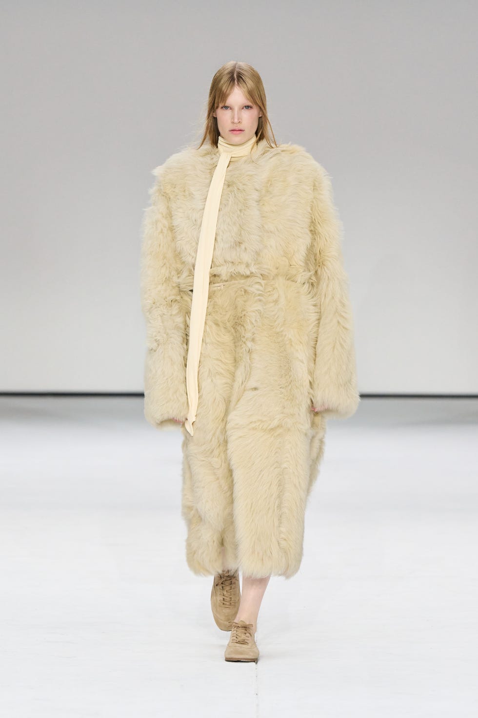 fashion model showcasing a plush fur coat with a belt and a lightcolored tie