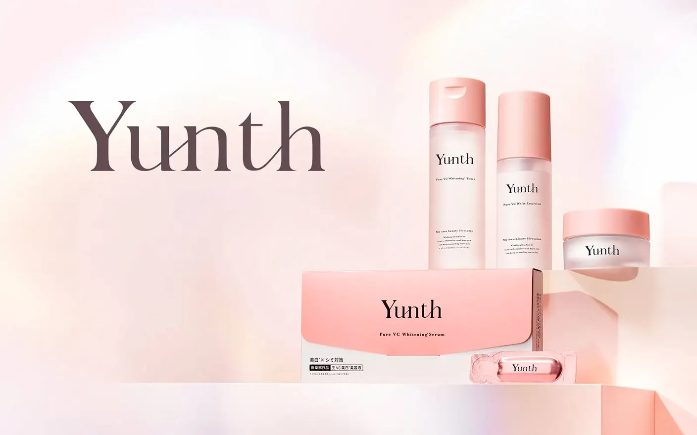 ピンク色の化粧品がいくつか並べられた画像です。化粧品には「Yunth」のロゴが入っており、「Pure VC Whitening Serum」や「Pure VC White Emulsion」などの商品名が記載されています。
