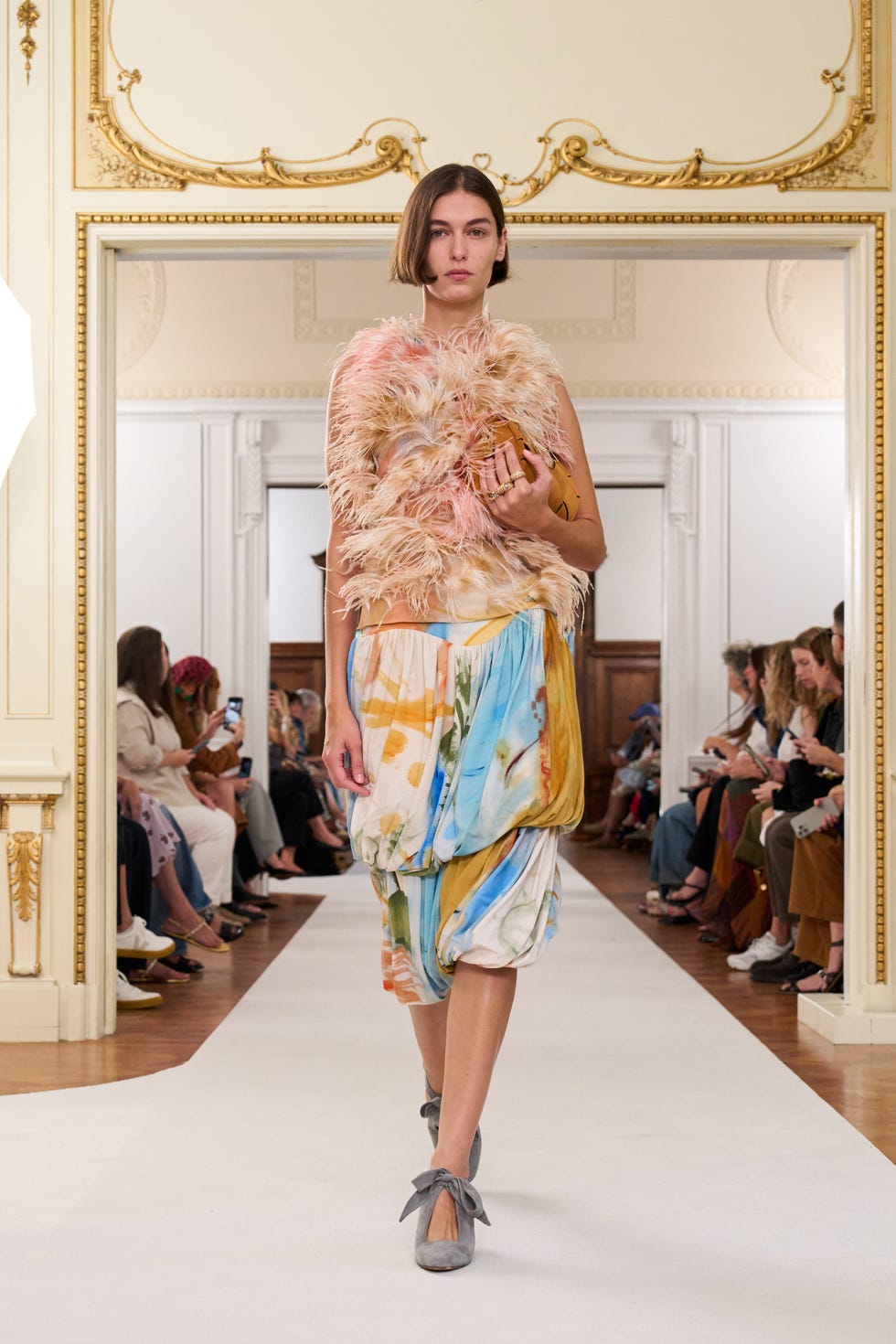 fashion model walking the runway in a feathered top and colorful skirt