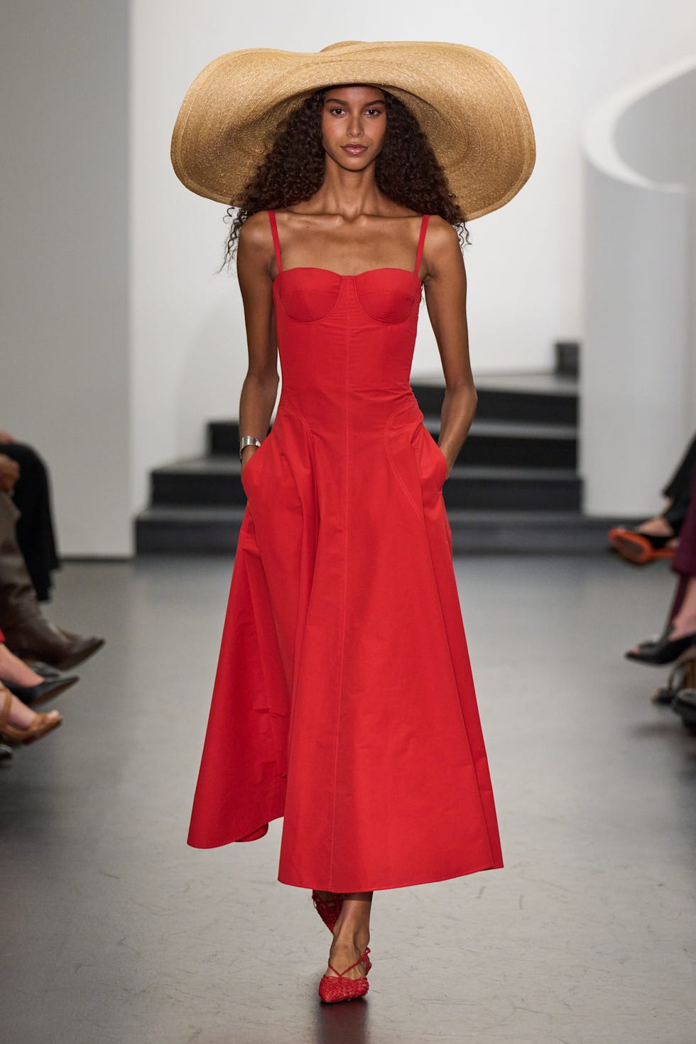 model showcasing a red dress and a large straw hat on a runway