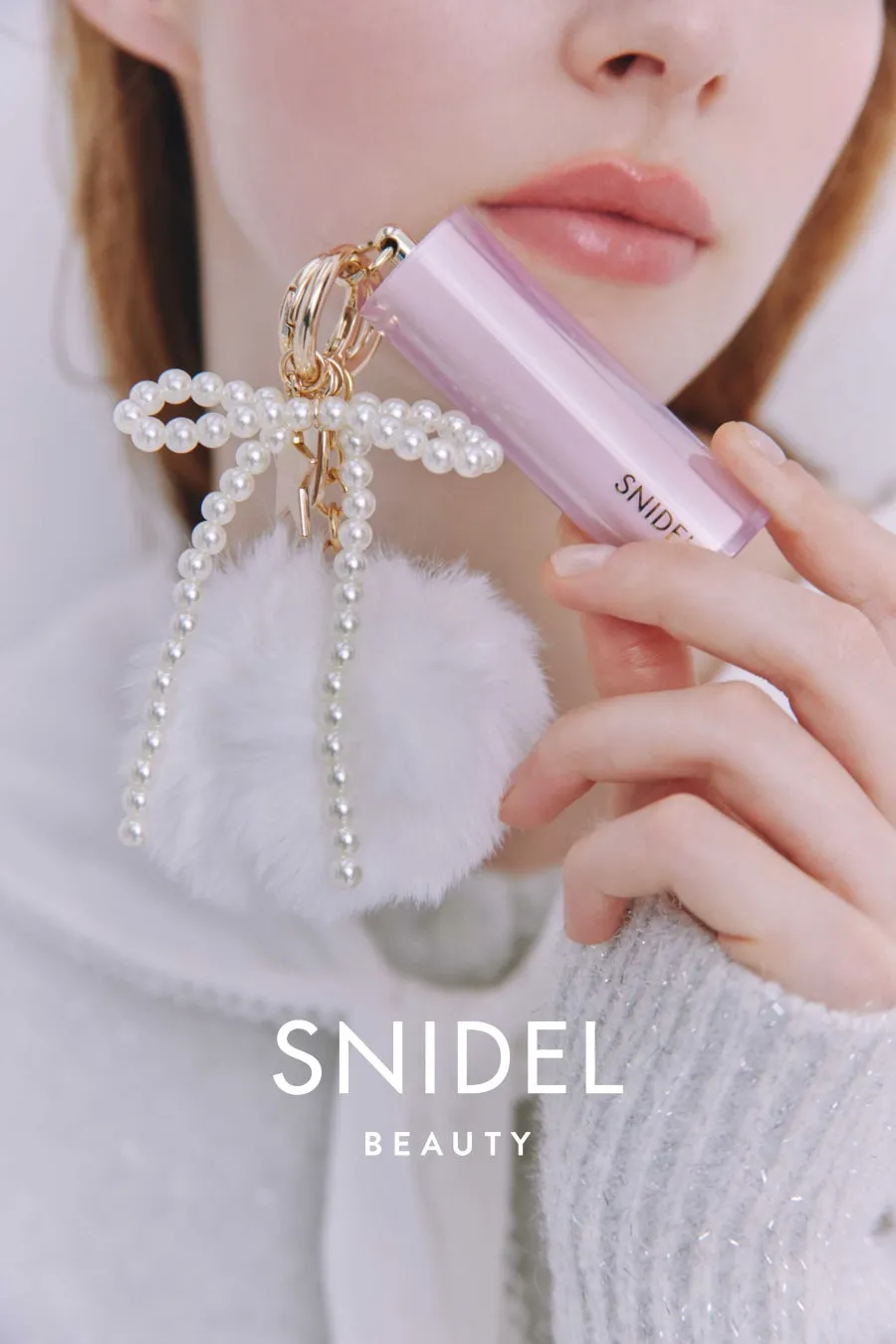 女性がリップスティックとアクセサリーを持ったポートレート。リップスティックのブランドはSNIDEL。アクセサリーは真珠と白いファーボールで構成されている。