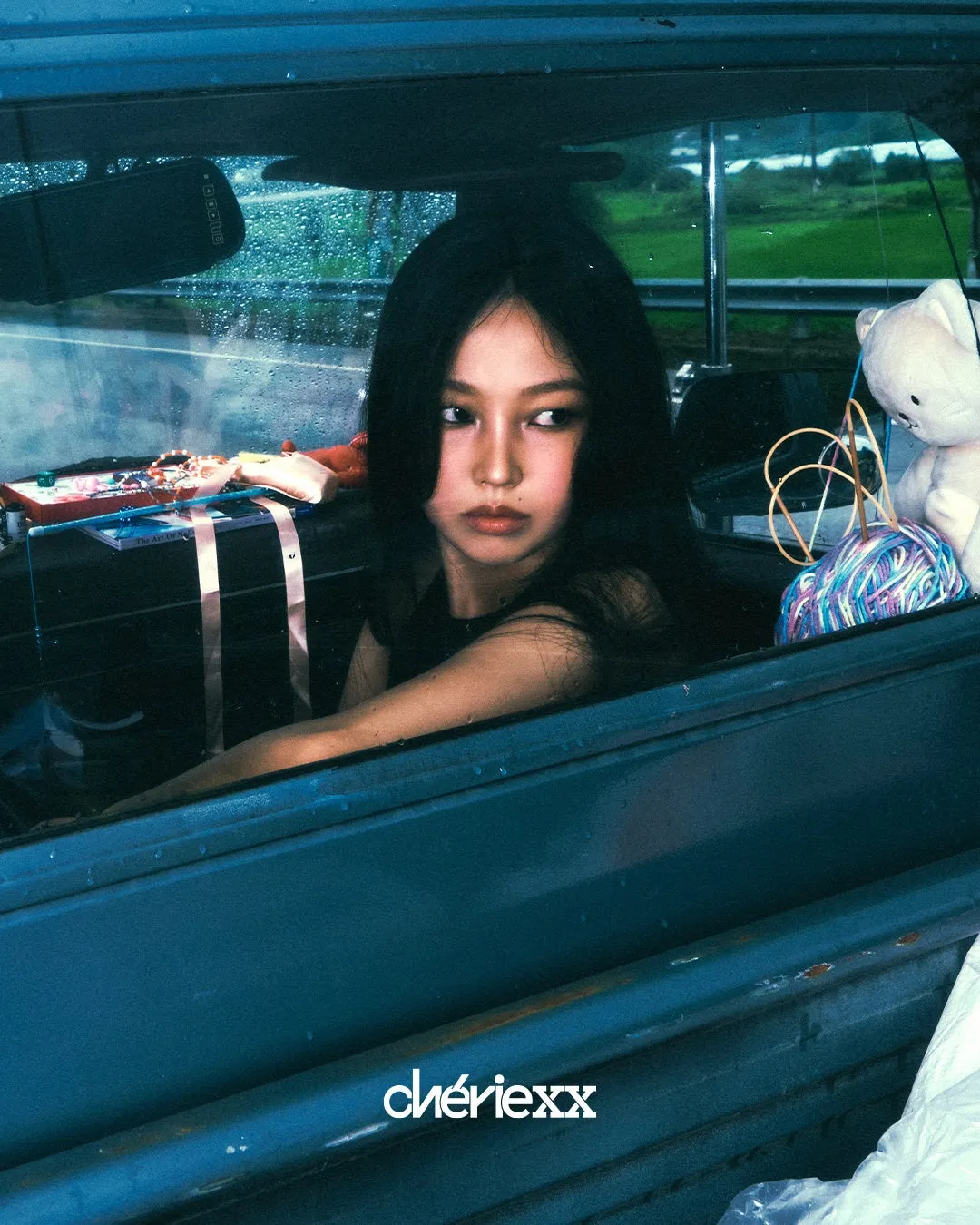 車の中に座っている女性のポートレート。窓から雨が降っているのが見える。女性はカメラを見つめている。