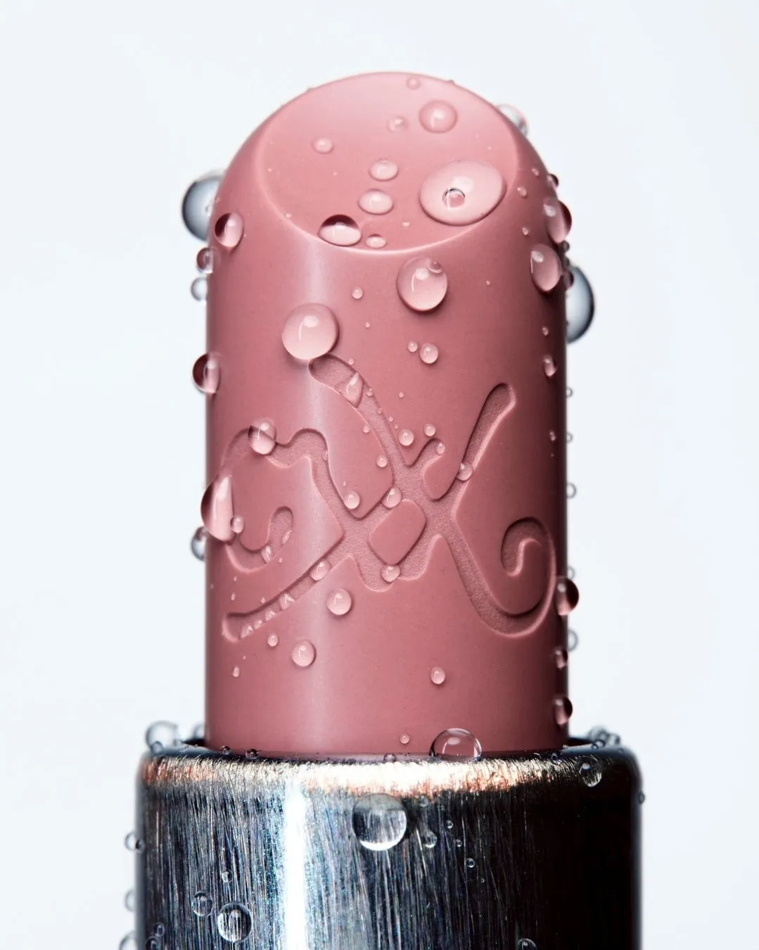 ピンク色のリップスティックに水滴が付着したクローズアップ写真。リップスティックには「FX」の文字が刻まれている。