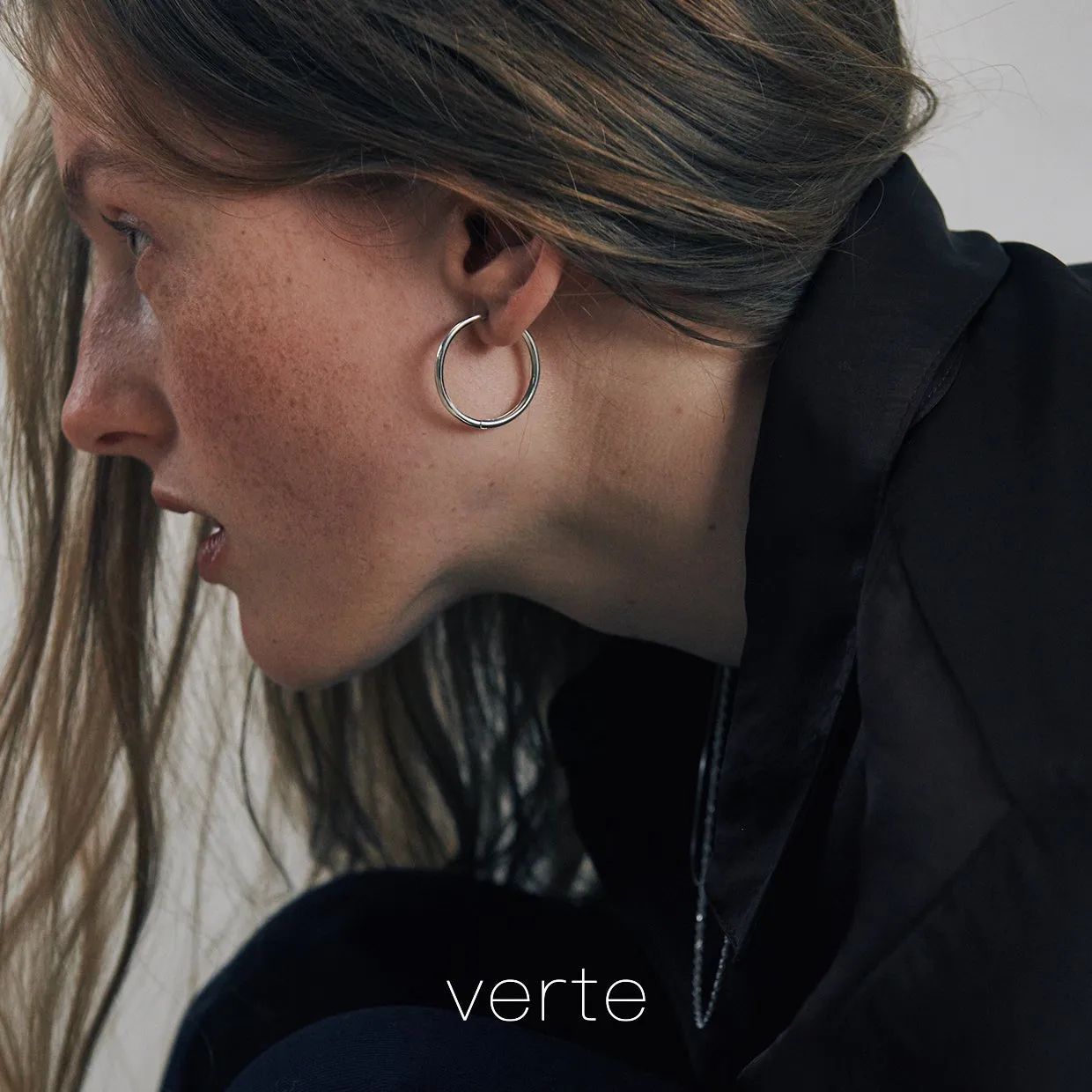 女性の横顔、銀色のフープピアス、黒い服。ブランド名「verte」が画像下部に表示。