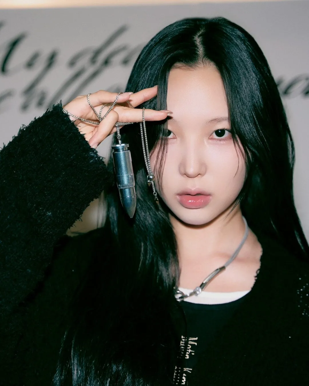 黒い服を着て、銀色のネックレスとペンダントを手に持っている女性のポートレート。彼女はカメラを見つめています。