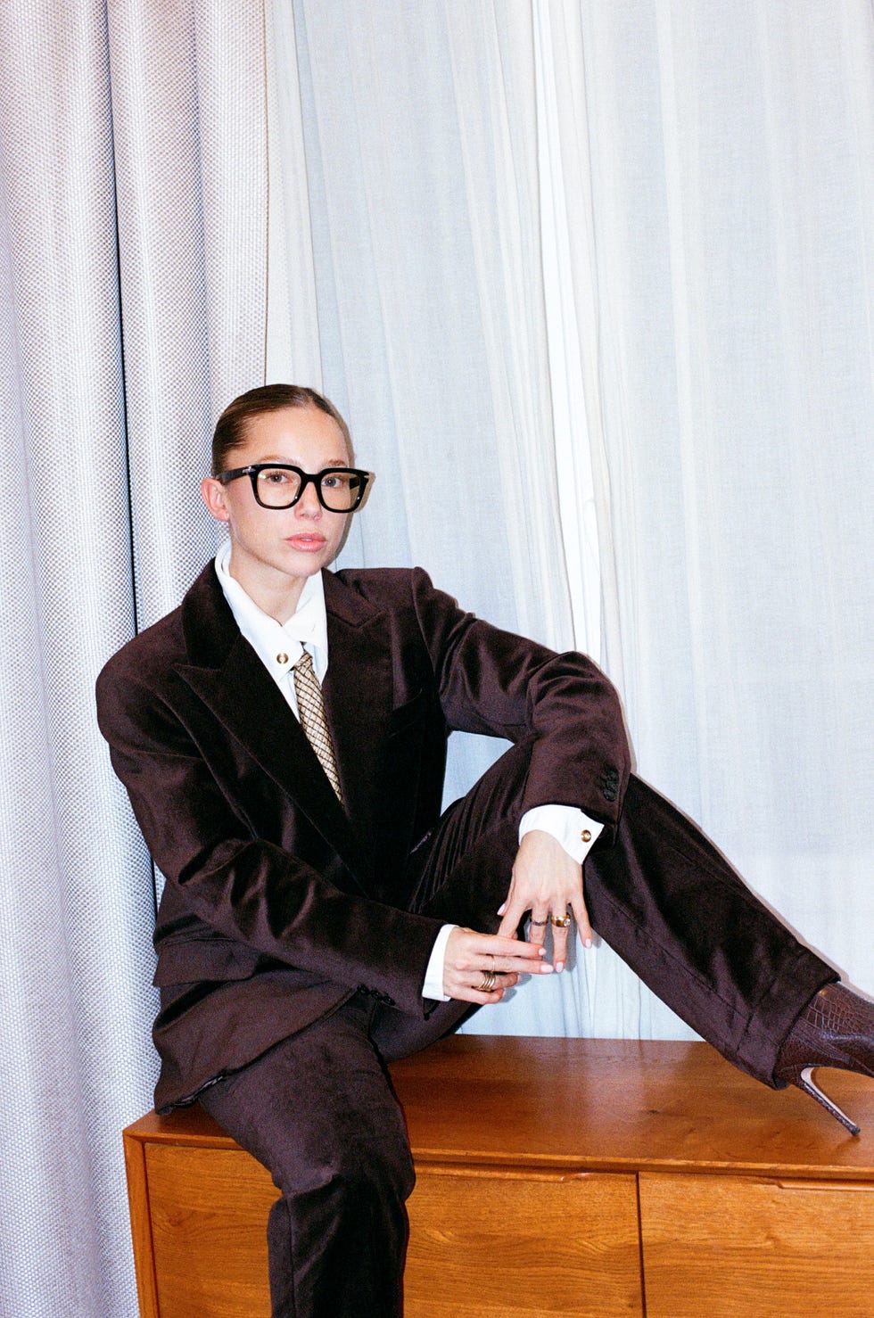 person in formal attire poses on a wooden surface with a stylish background