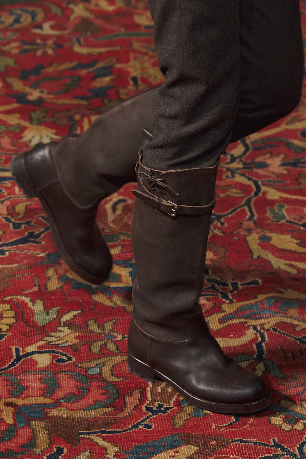 foot wearing a kneehigh brown boot on a patterned rug