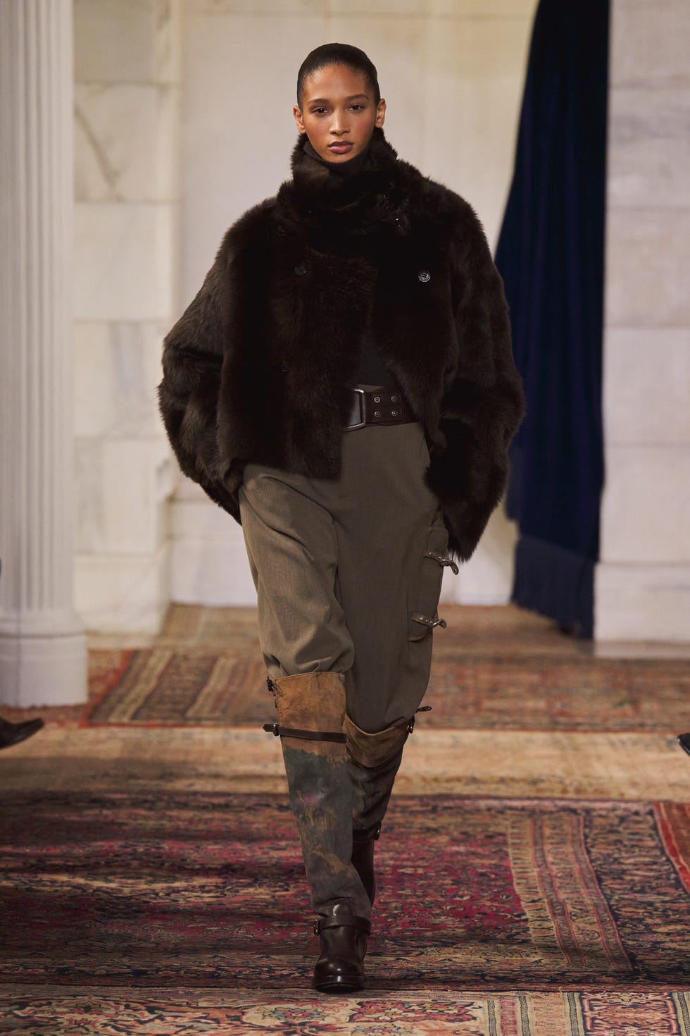 fashion model showcasing an outfit with a fur coat and cargo pants on a runway