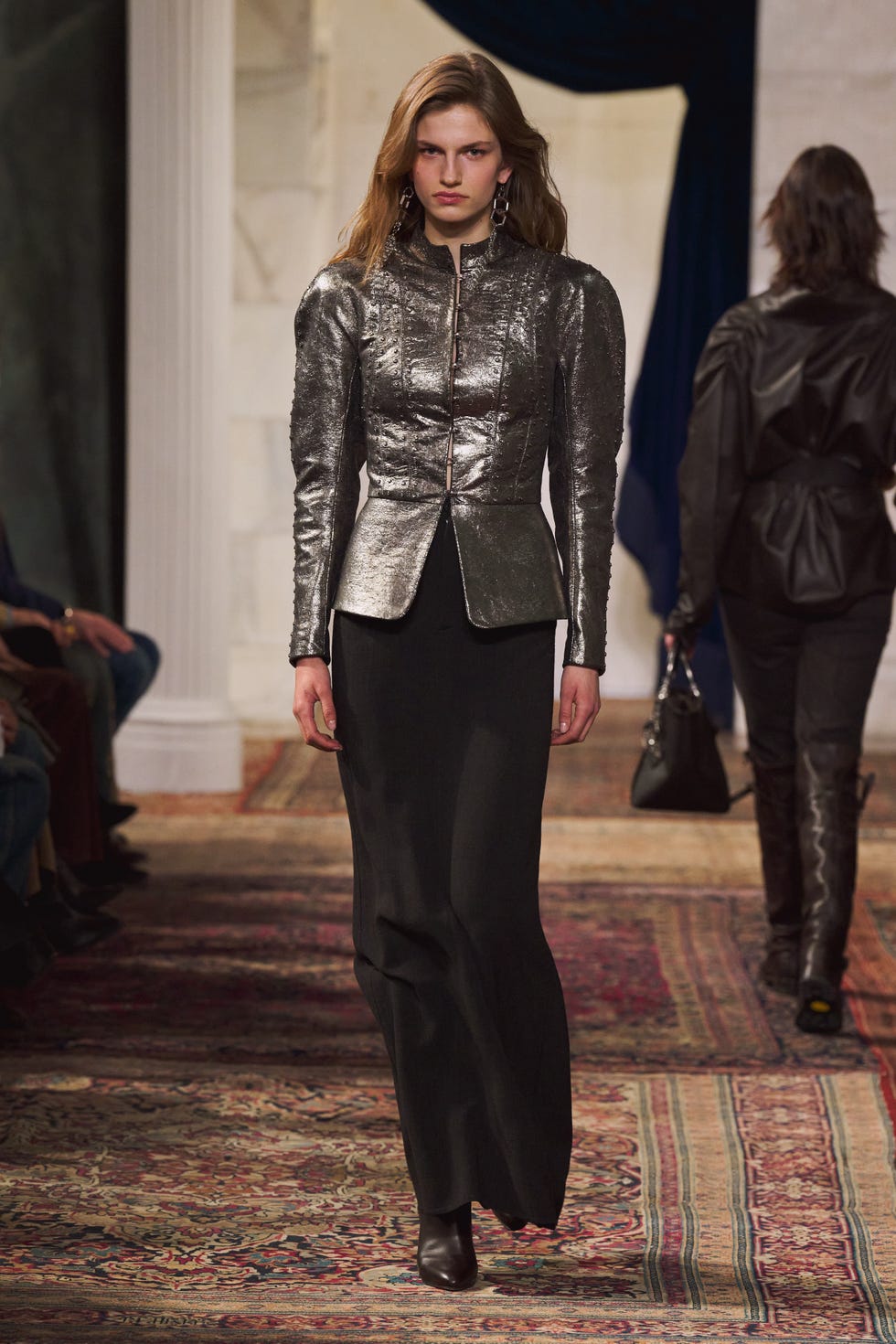 fashion model on runway showcasing a metallic jacket and long black skirt