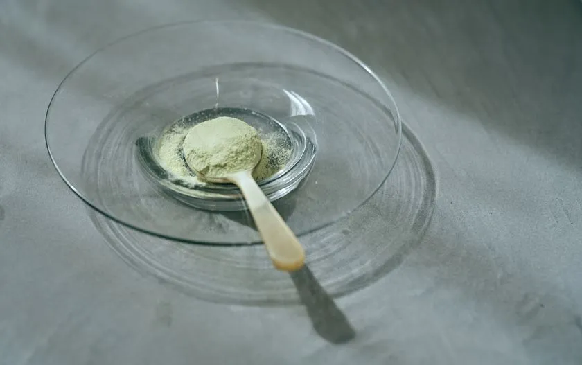 抹茶色のプロテインパウダーを木製スプーンですくった接写