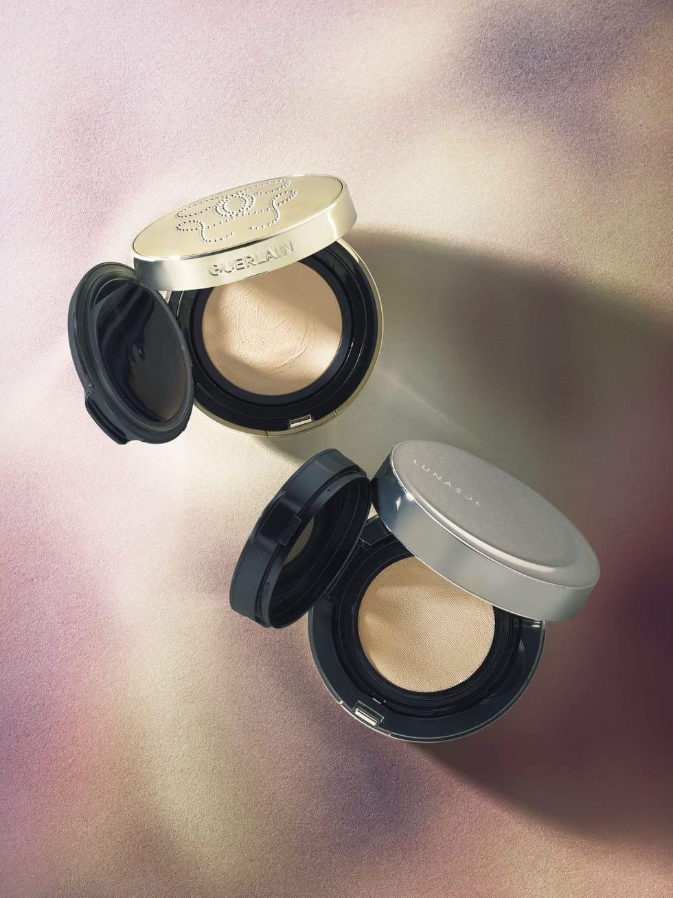 two opened compacts of foundation on a soft gradient background