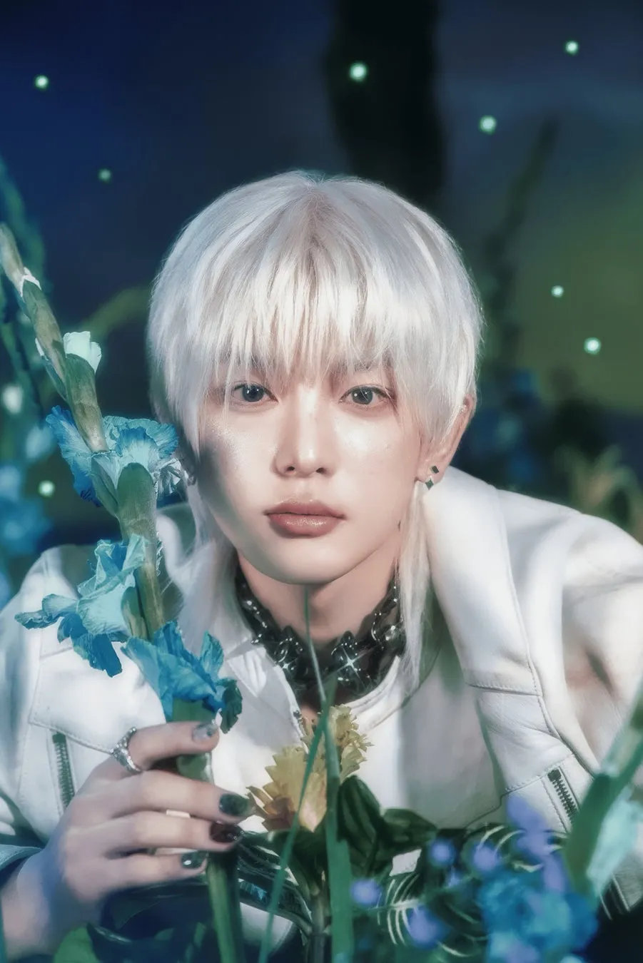 &TEAM HARUAが花王「est」スペシャルパートナーに初就任!本人コメントあり!限定ステッカー付き「砂漠スキンケア」で美肌を掴む 5 白髪の男性が花に囲まれてポーズを取っている様子を描いた写真。彼は白いジャケットを着ており、顔の近くには青い花が咲いています。背景は暗く、緑の光が散りばめられています。