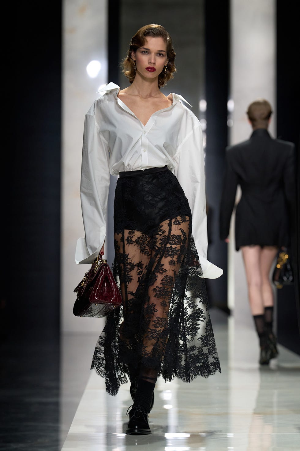 model on runway wearing a white shirt and black lace skirt