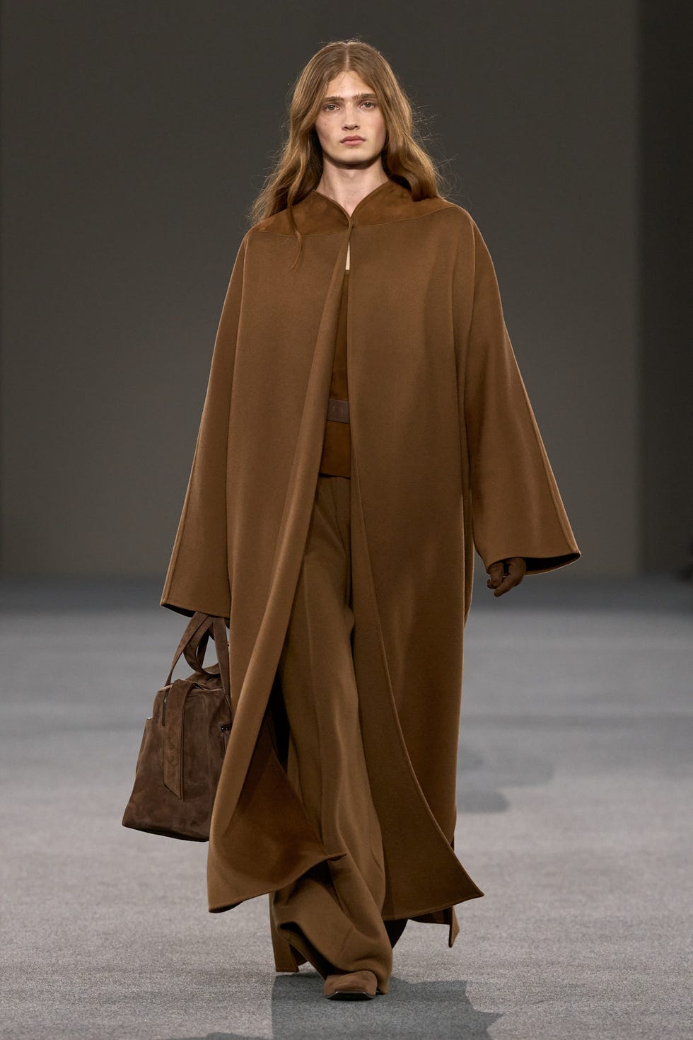 runway model showcasing a fashionable outfit with a brown cape and matching pants