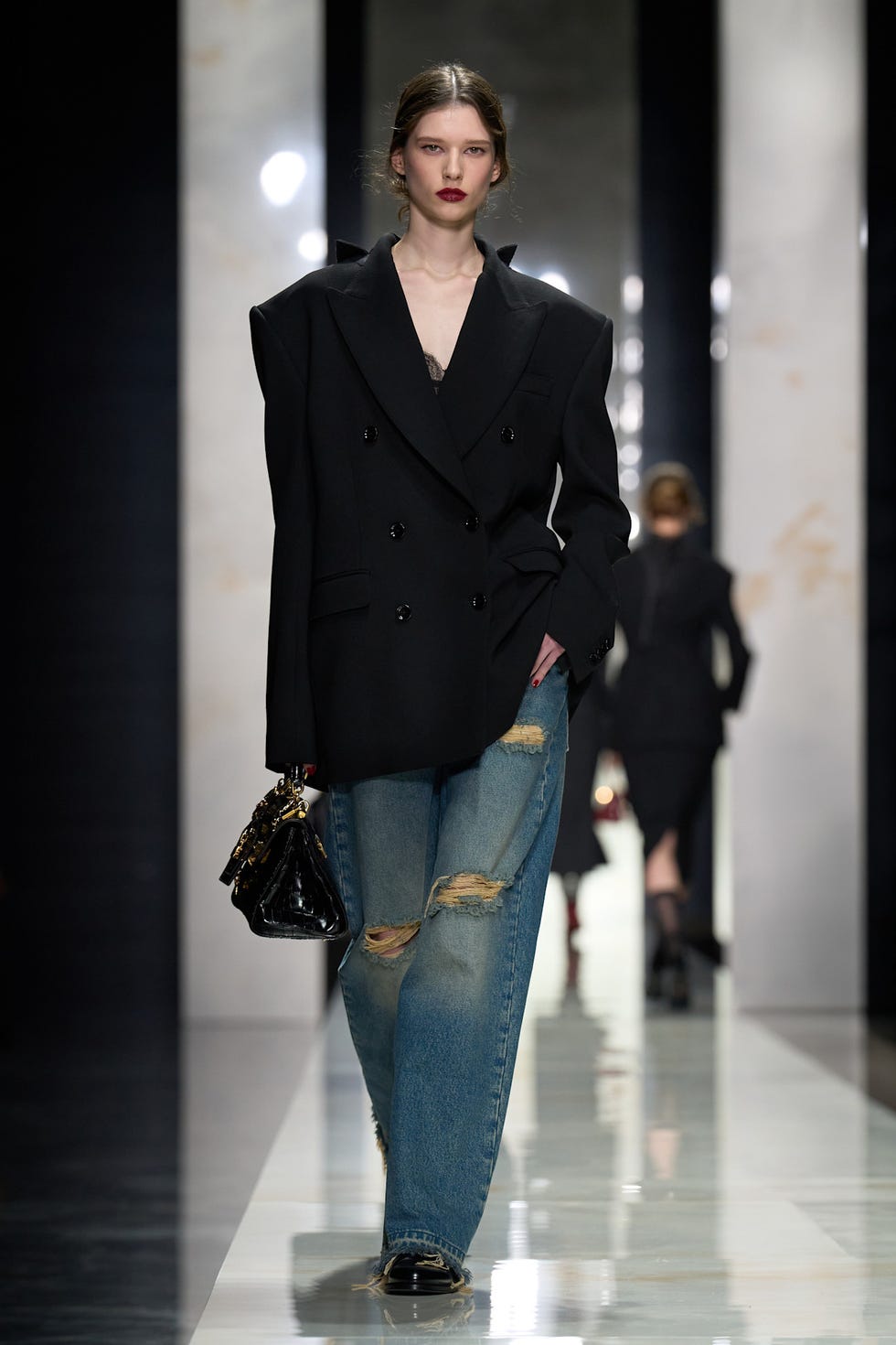 fashion model on the runway wearing an oversized black blazer and distressed denim jeans