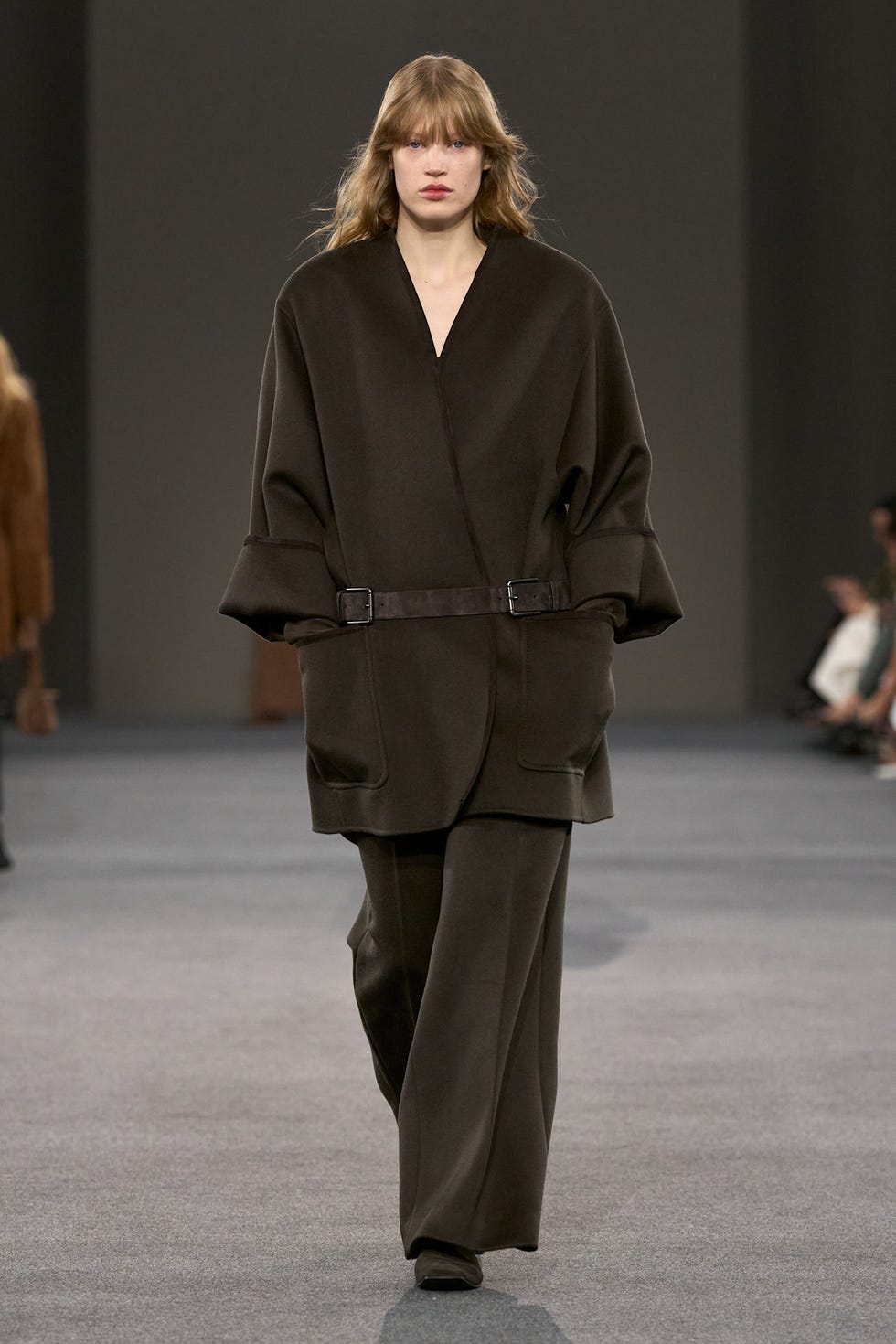 fashion model walking on a runway wearing a brown oversized outfit