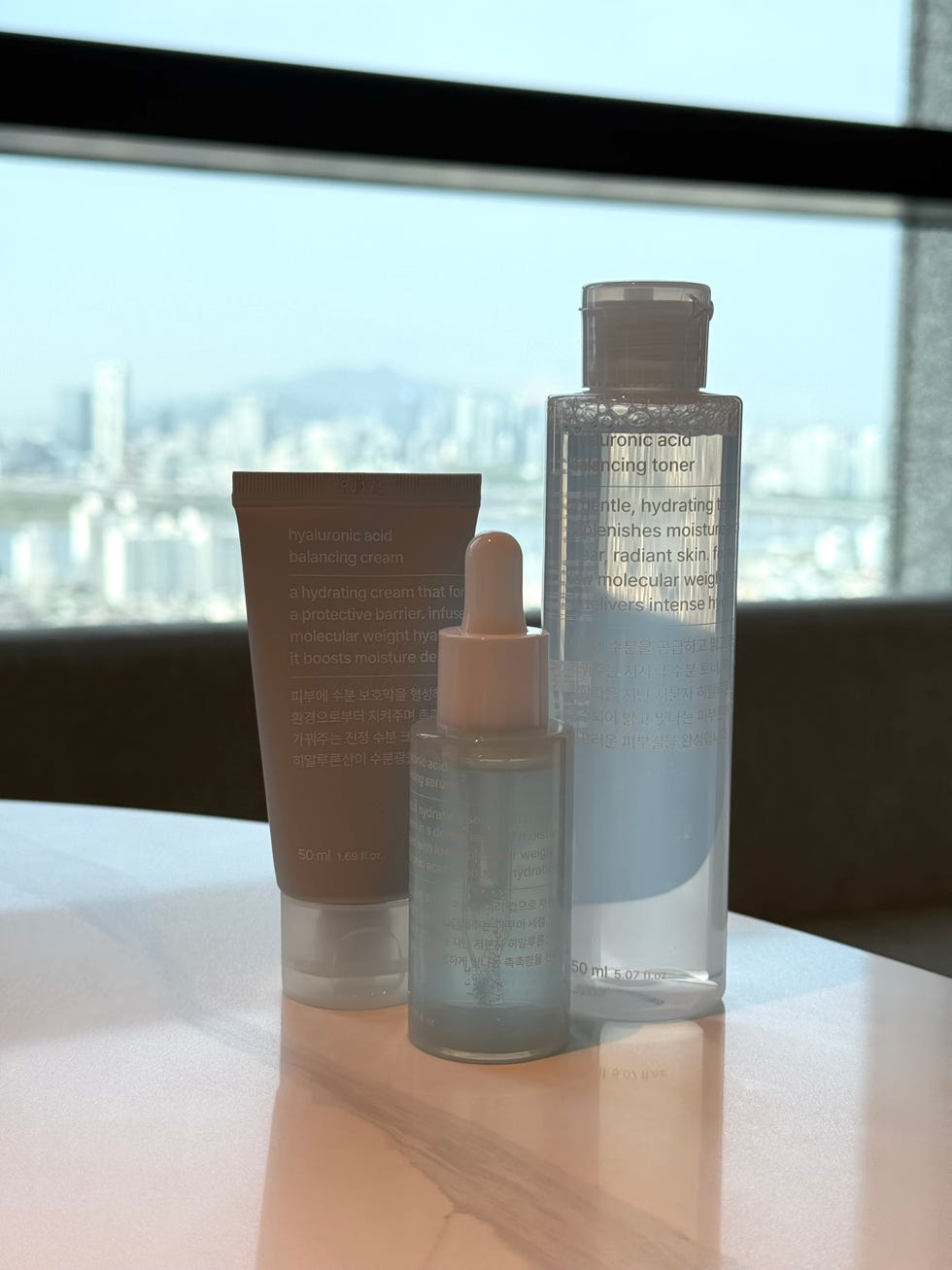 three skincare products displayed on a countertop with a city view in the background three skincare products displayed on a countertop with a city view in the background
